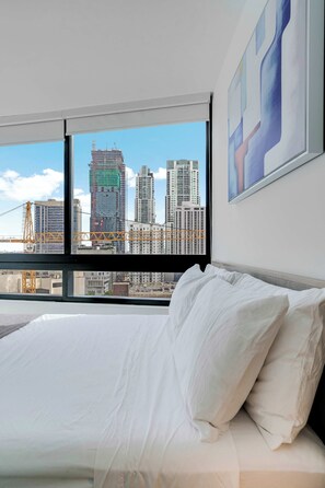 A hotel room with a large bed, a view of a city skyline, and a framed abstract painting on the wall. - Sleek Escape Resort-style Stay With Pool & Parking (Miami)