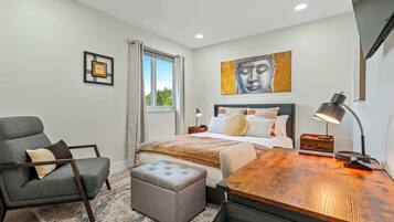 Une chambre à coucher comprenant un lit, une chaise, un bureau, une lampe, une fenêtre avec des rideaux, un tableau au mur et une petite table.