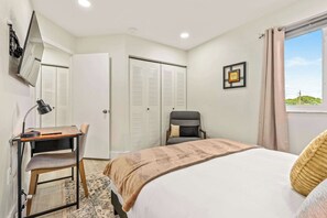 A bedroom with a bed, a desk with a chair, a wardrobe, and a window with curtains.