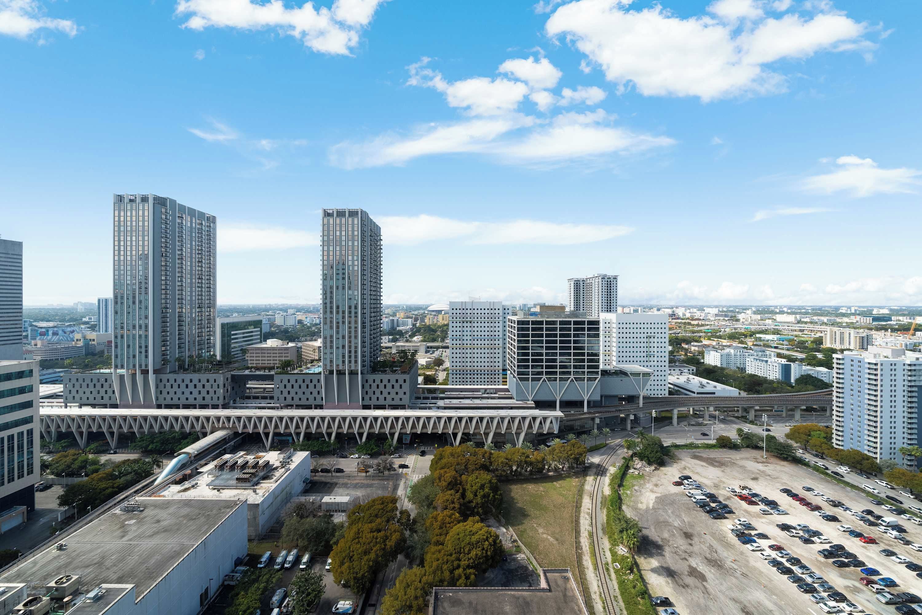 A high-rise urban area with modern buildings, a parking lot, and a bridge.