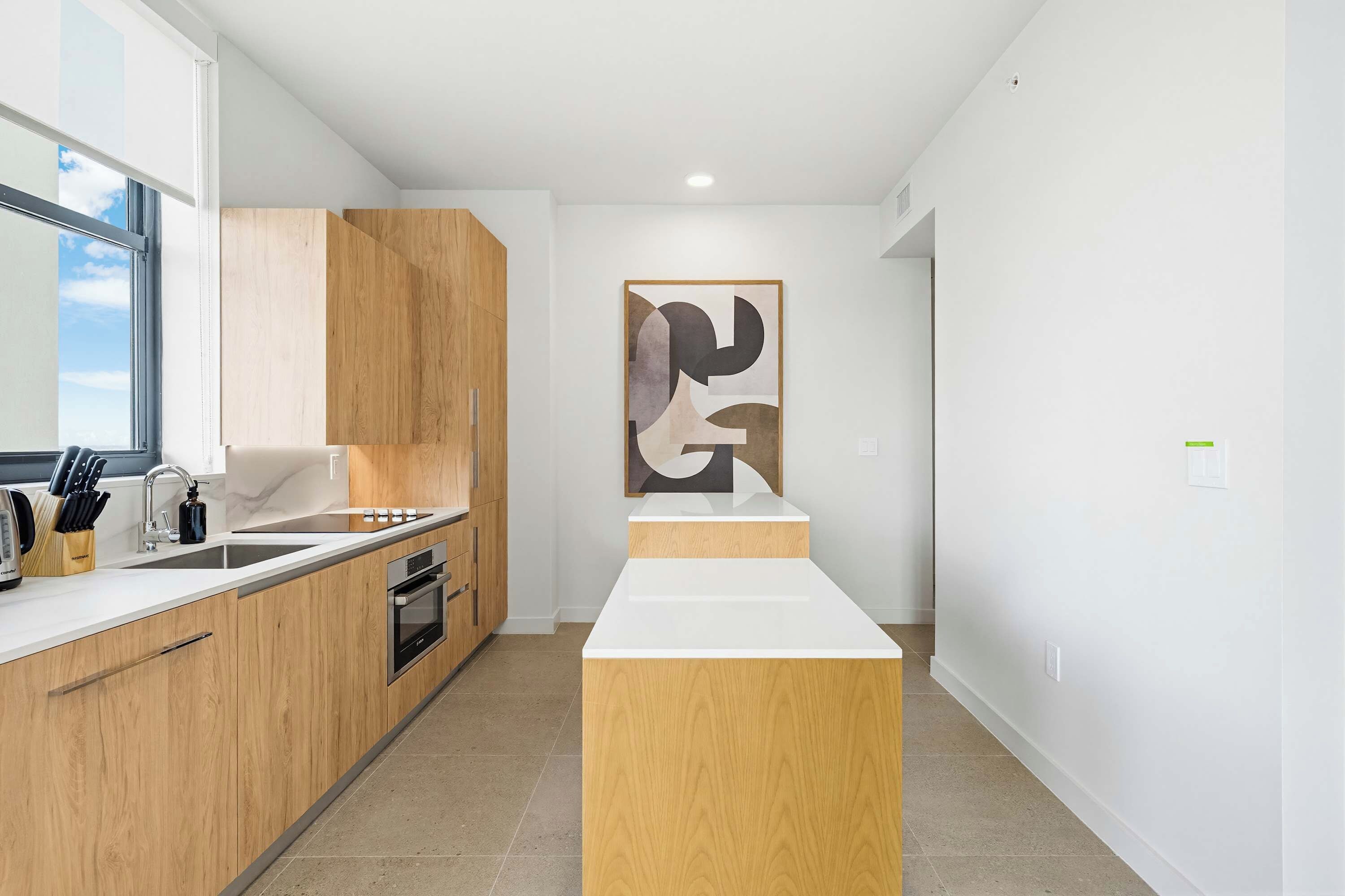 A modern kitchen with wooden cabinets, a white countertop, and a large abstract painting on the wall.