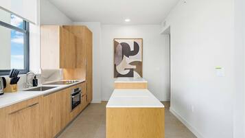 A modern kitchen with wooden cabinets, a white countertop, and a large abstract painting on the wall.
