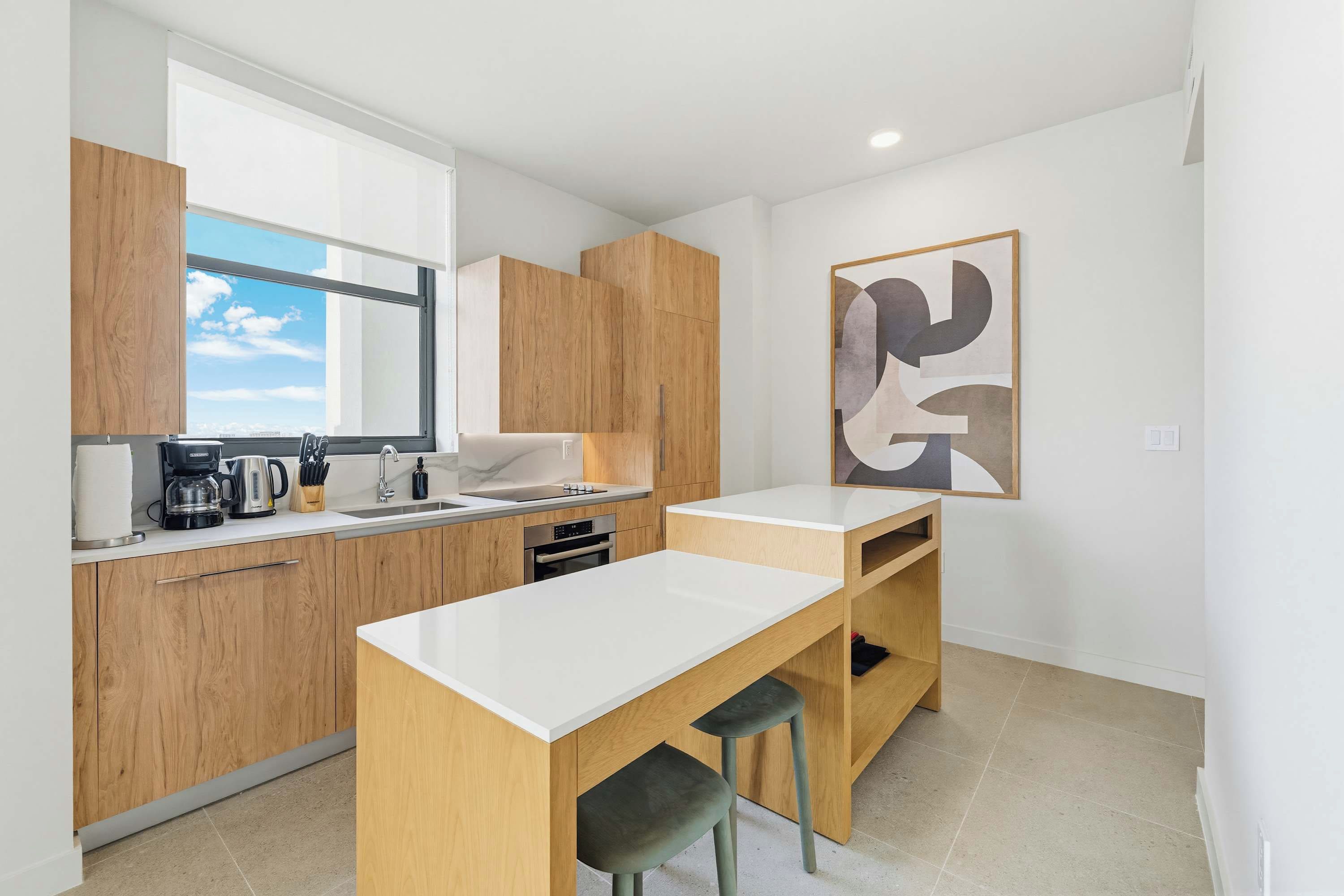 A modern kitchen with wooden cabinets, a white countertop, and a large window.
