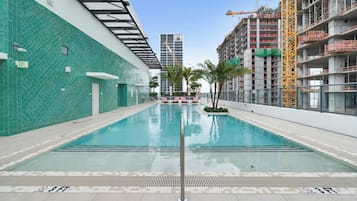 A swimming pool with a 3 FT depth marker, surrounded by a building with a green tiled exterior and a construction crane in the background.