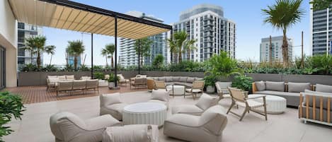 A rooftop patio with outdoor furniture, palm trees, and modern buildings in the background.