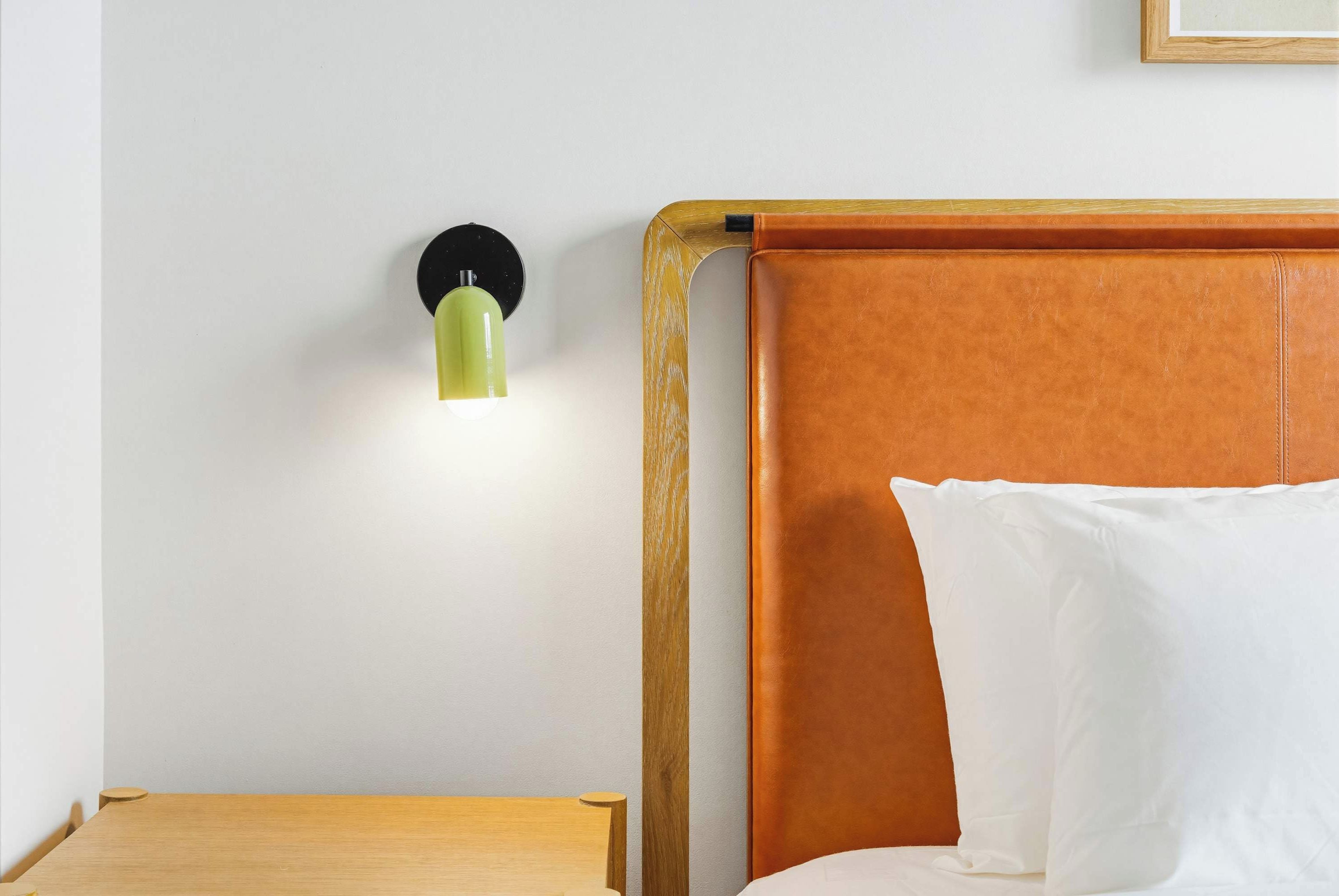 A bedroom with a wooden headboard, a bedside table, and a wall-mounted light fixture.