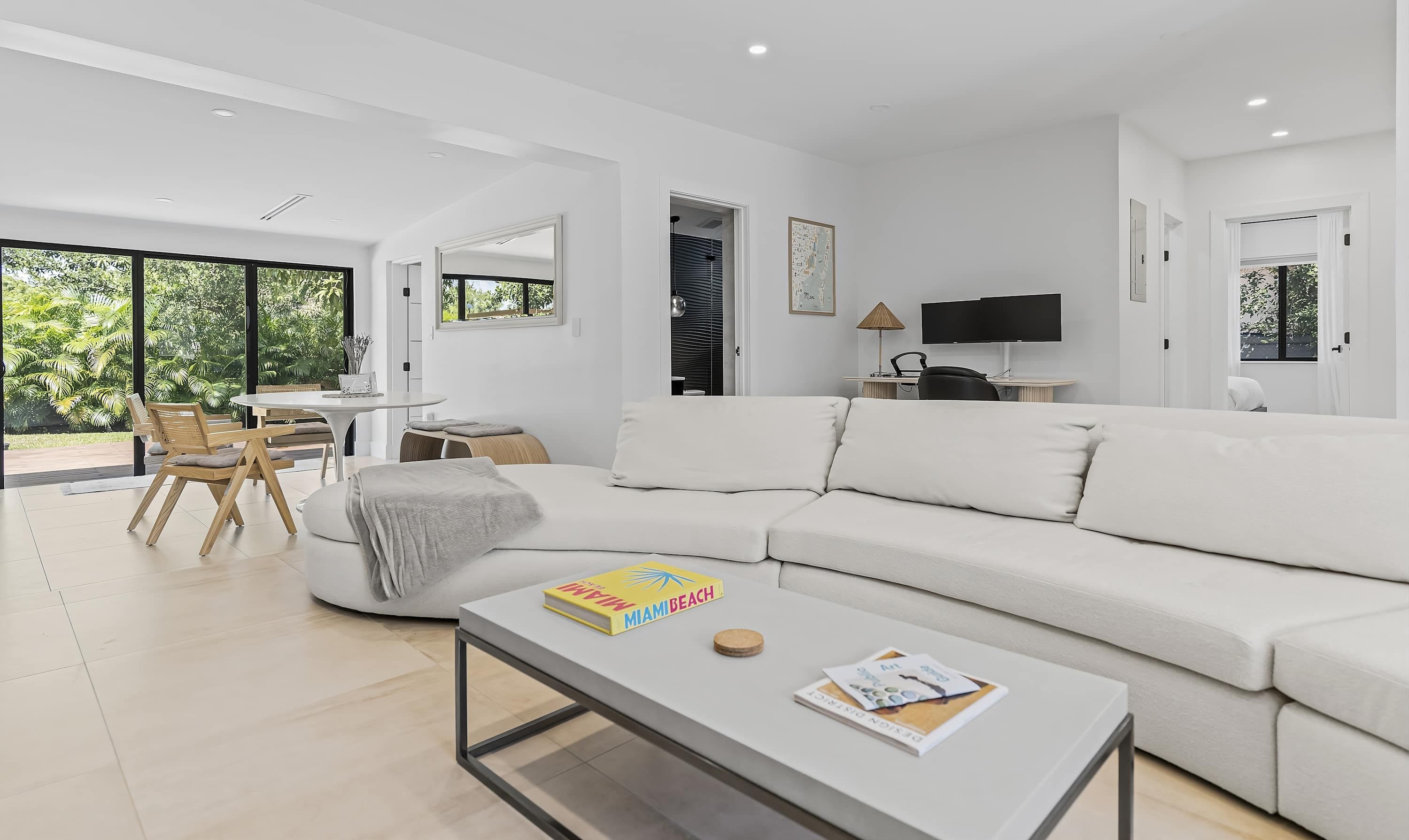Una sala de estar moderna con un sofá blanco, una mesa de centro y una zona de comedor con sillas y una mesa de madera.