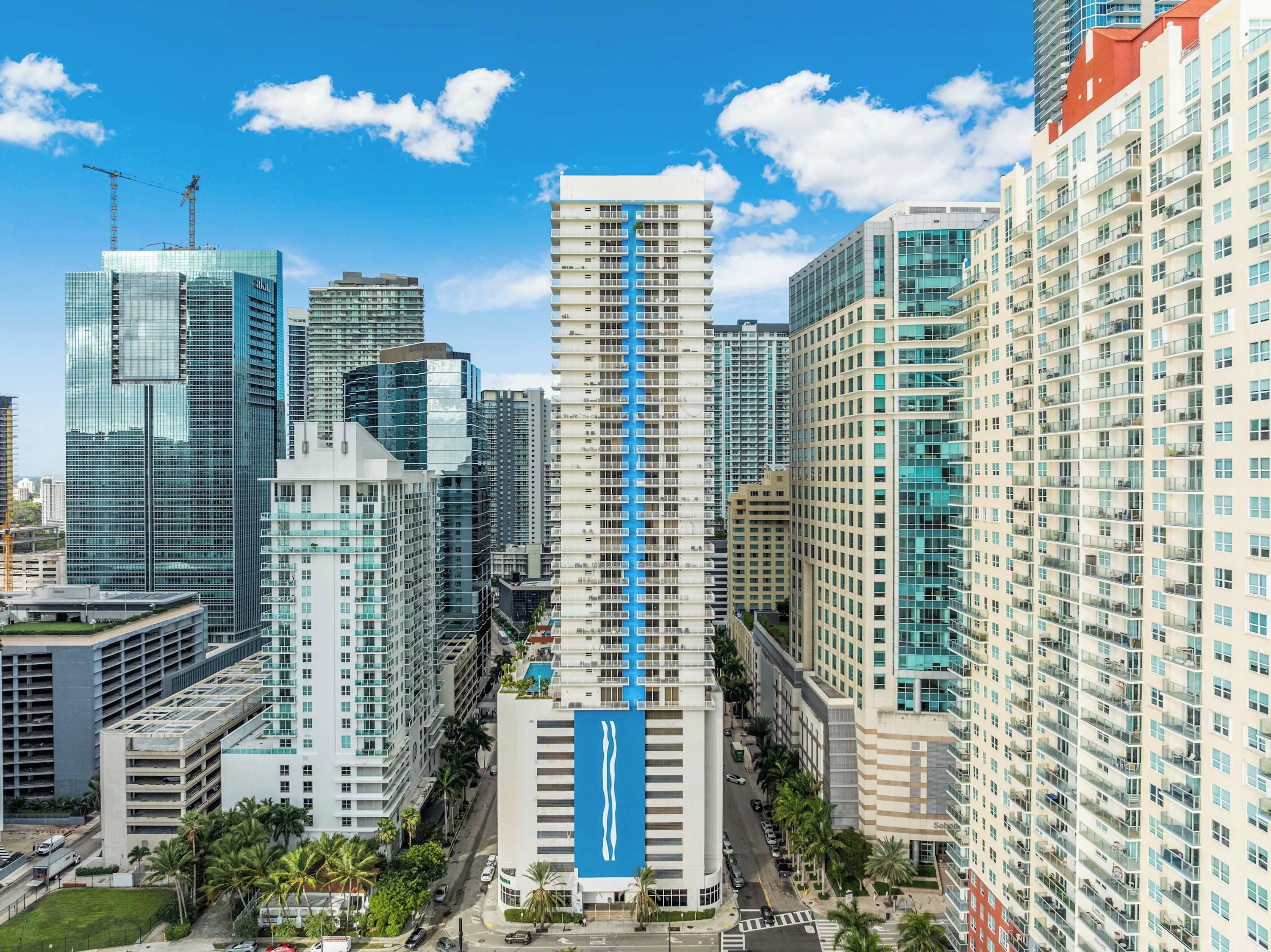 A high-rise building with a prominent blue vertical stripe, surrounded by other tall buildings in a cityscape.