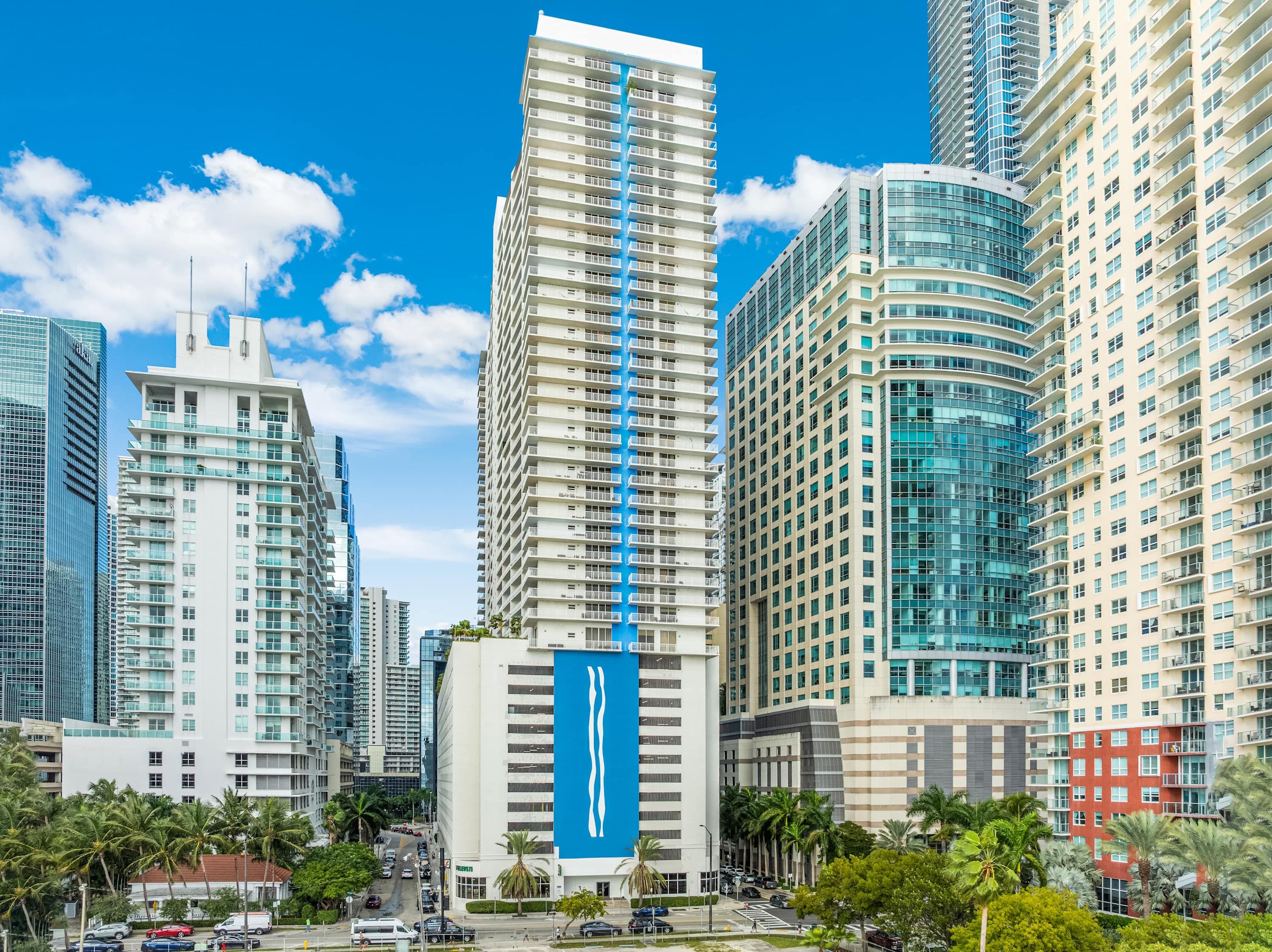 Un paysage urbain avec des immeubles modernes de grande hauteur, dont un bâtiment blanc remarquable orné d’une bande verticale bleue et un bâtiment aux façades courbes en verre.