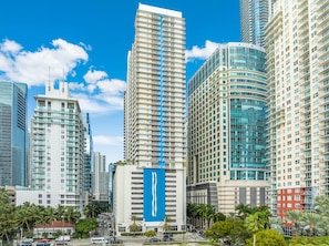 A cityscape with modern high-rise buildings, including a prominent white building with a blue vertical stripe and a curved glass building. - Brickell Bay View Unbeatable Location and Parking (Miami)