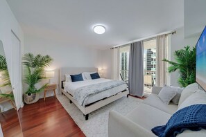 Quarto moderno com uma cama grande, um sofá e uma varanda com vista para a cidade.