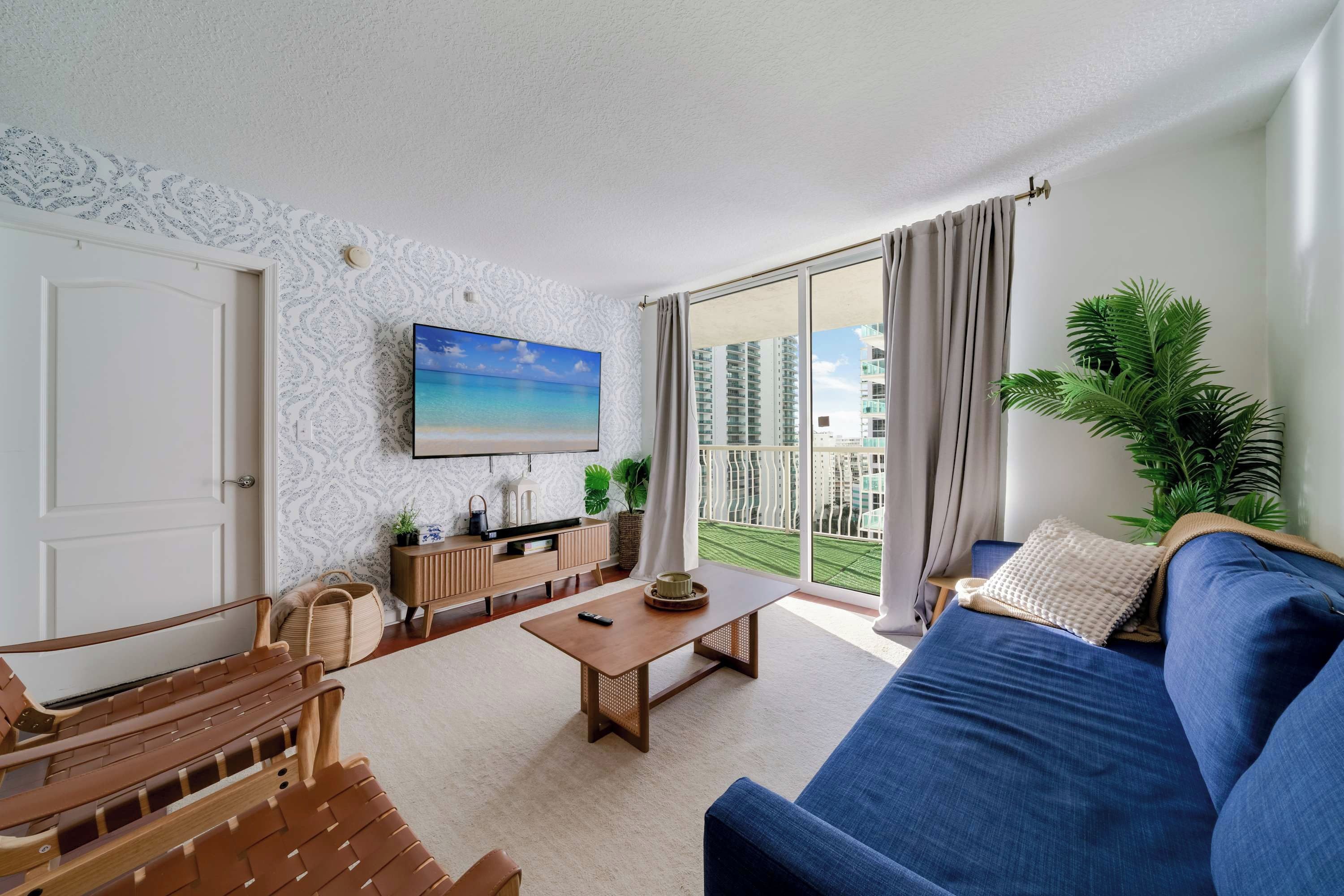 Ein Wohnzimmer mit einem blauen Sofa, einem Holztisch und einem an der Wand befestigten Fernseher.
