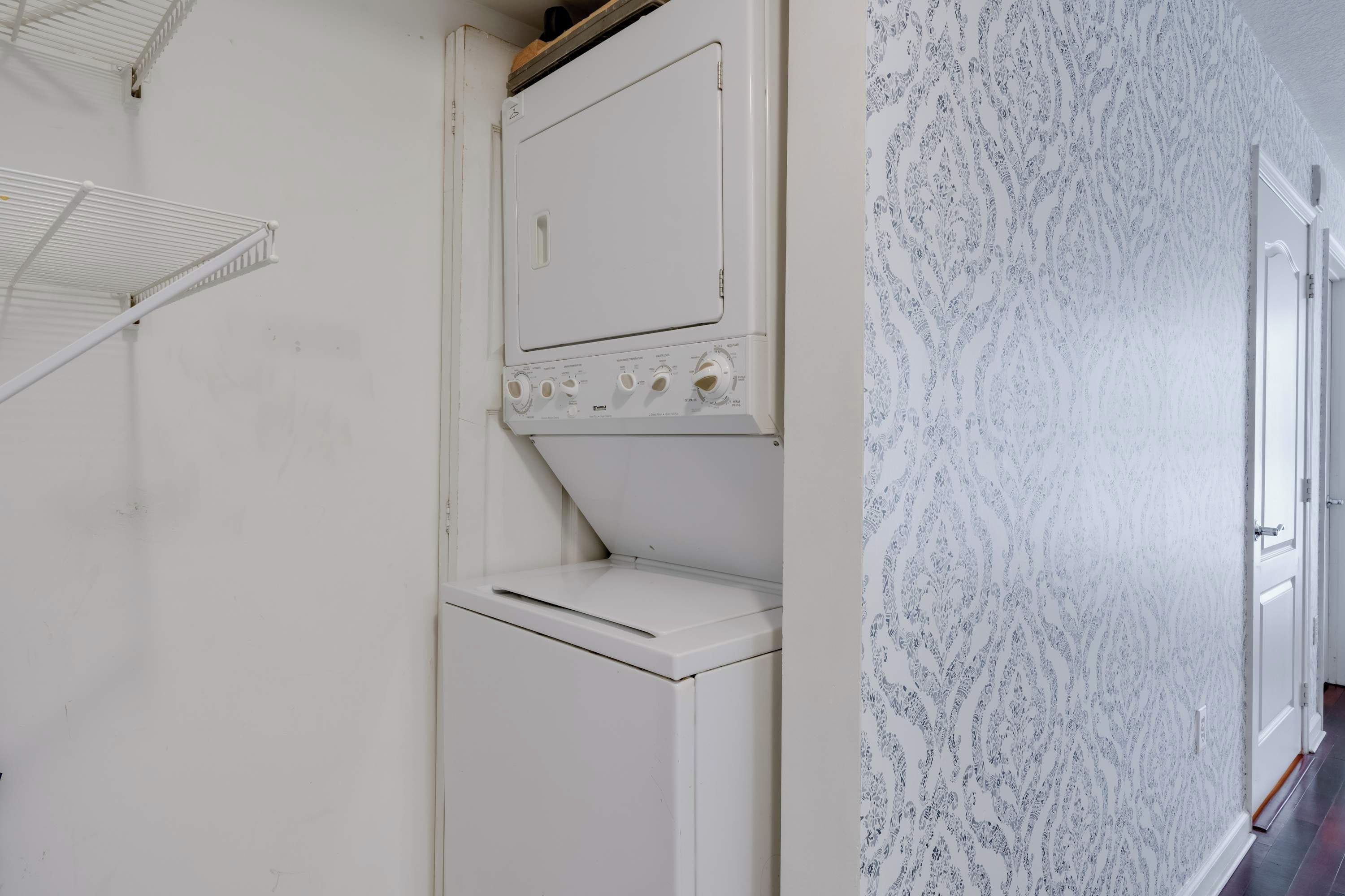A laundry room with a white washing machine and dryer, a metal shelf, and patterned wallpaper.