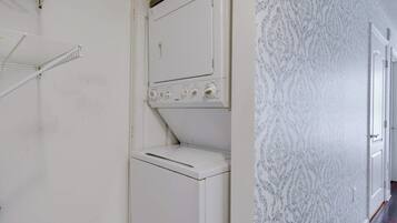 A laundry room with a white washing machine and dryer, a metal shelf, and patterned wallpaper.