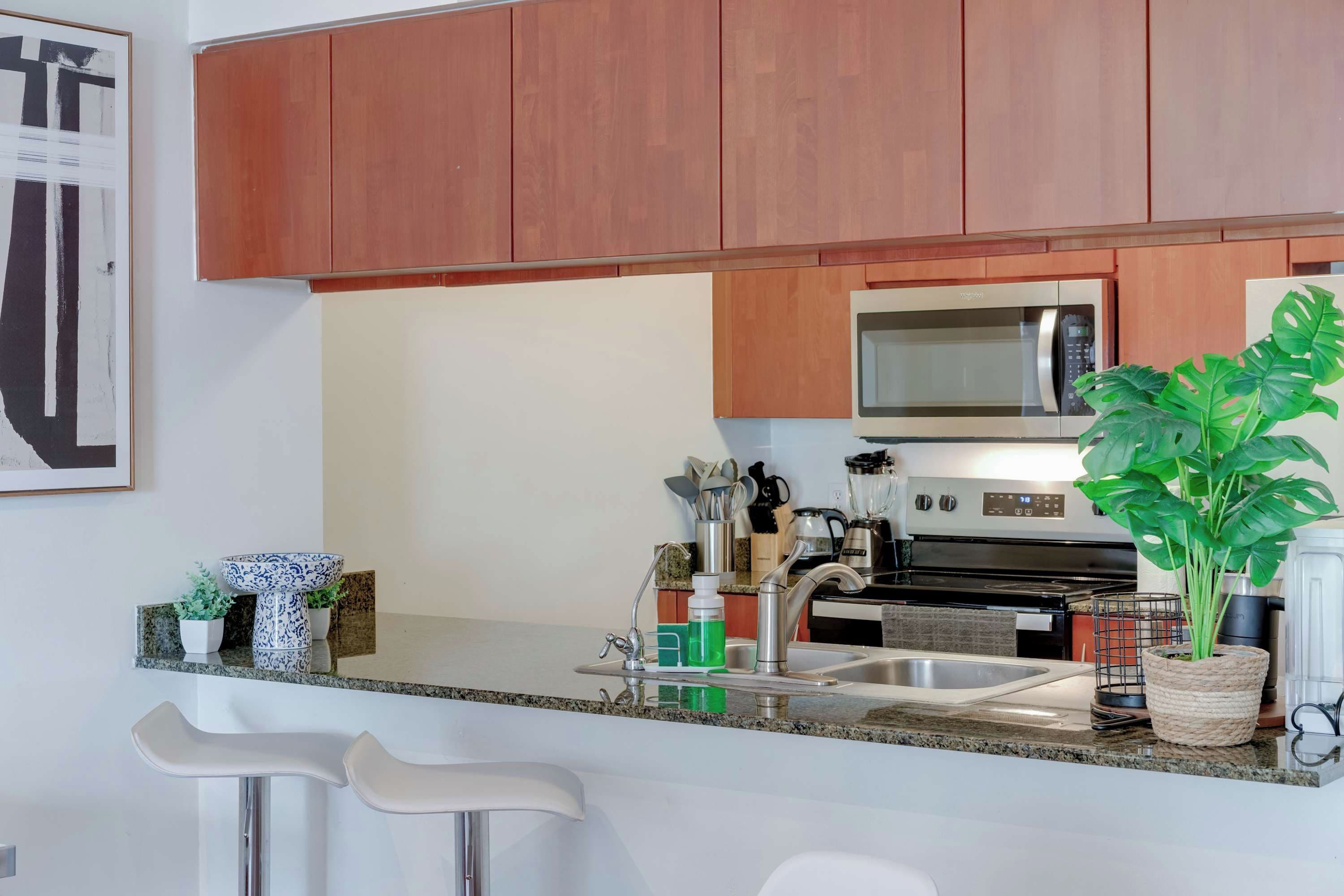 Una cucina moderna con mobili in legno, un forno a microonde in acciaio inossidabile, un lavello e un angolo bar con sgabelli.