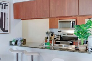 Cuina moderna amb armaris de fusta, microones d'acer inoxidable, un rentaplat i zona de bar amb tamborets.
