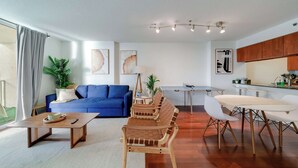 A modern living room with a blue sofa, wooden coffee table, and a dining area with a white table and chairs. - Brickell Bay View- Unbeatable Location and Parking (Miami)