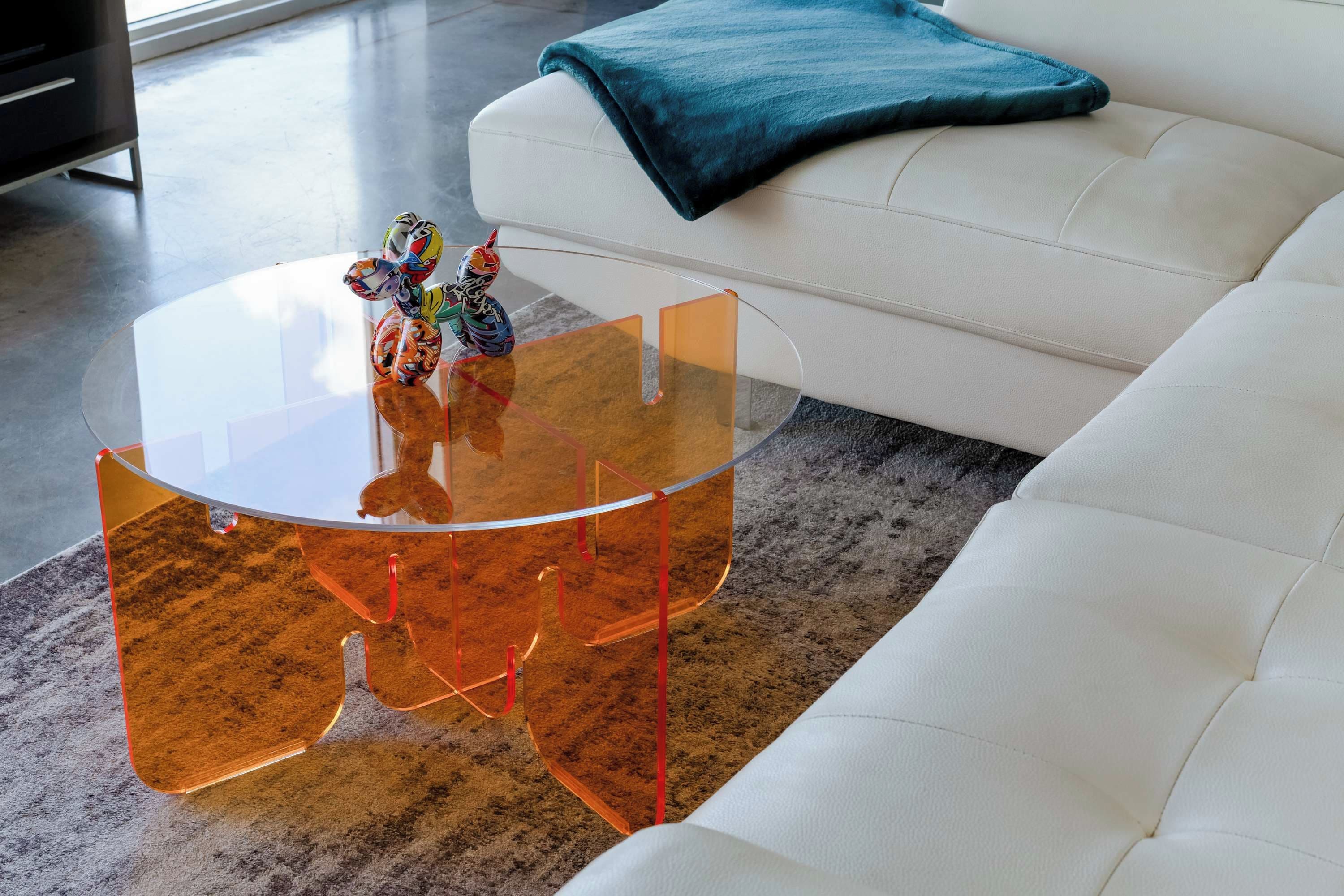 A modern living room with a white sofa, a glass coffee table with orange accents, and a colorful toy on the table.