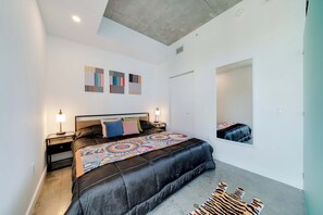 A modern bedroom with a large bed, two bedside tables with lamps, a large mirror, and abstract wall art. - Skyline Studio With Rooftop Pool & Parking (Miami)
