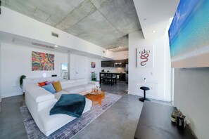 A modern living space with a white sofa, colorful cushions, a glass coffee table, and a kitchen area in the background. - Skyline Studio With Rooftop Pool & Parking (Miami)