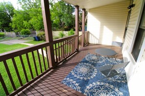 A covered porch with a wooden deck, a small table with chairs, and a patterned rug.