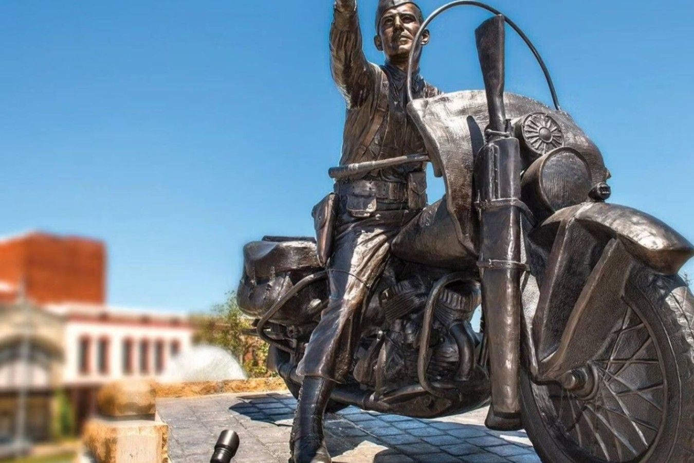 Une statue représentant une personne à moto, avec un ciel dégagé en arrière-plan.