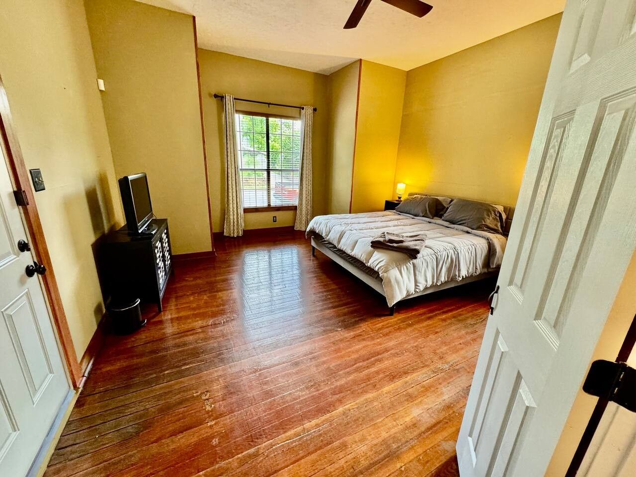 A bedroom with a bed, a dresser, a television, and a window with curtains.