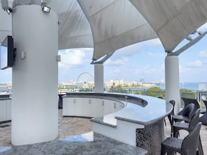Eine Dachterrasse mit einer gebogenen Bar, Außenbestuhlung und Blick auf ein Riesenrad und die Stadtlandschaft.