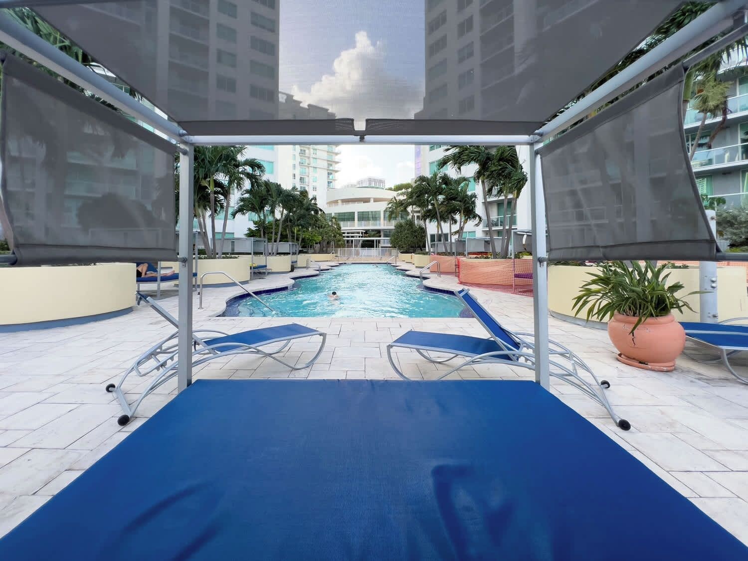 Ein Poolbereich mit blauen Liegestühlen, einer überdachten Lounge und Blick auf umliegende Gebäude.