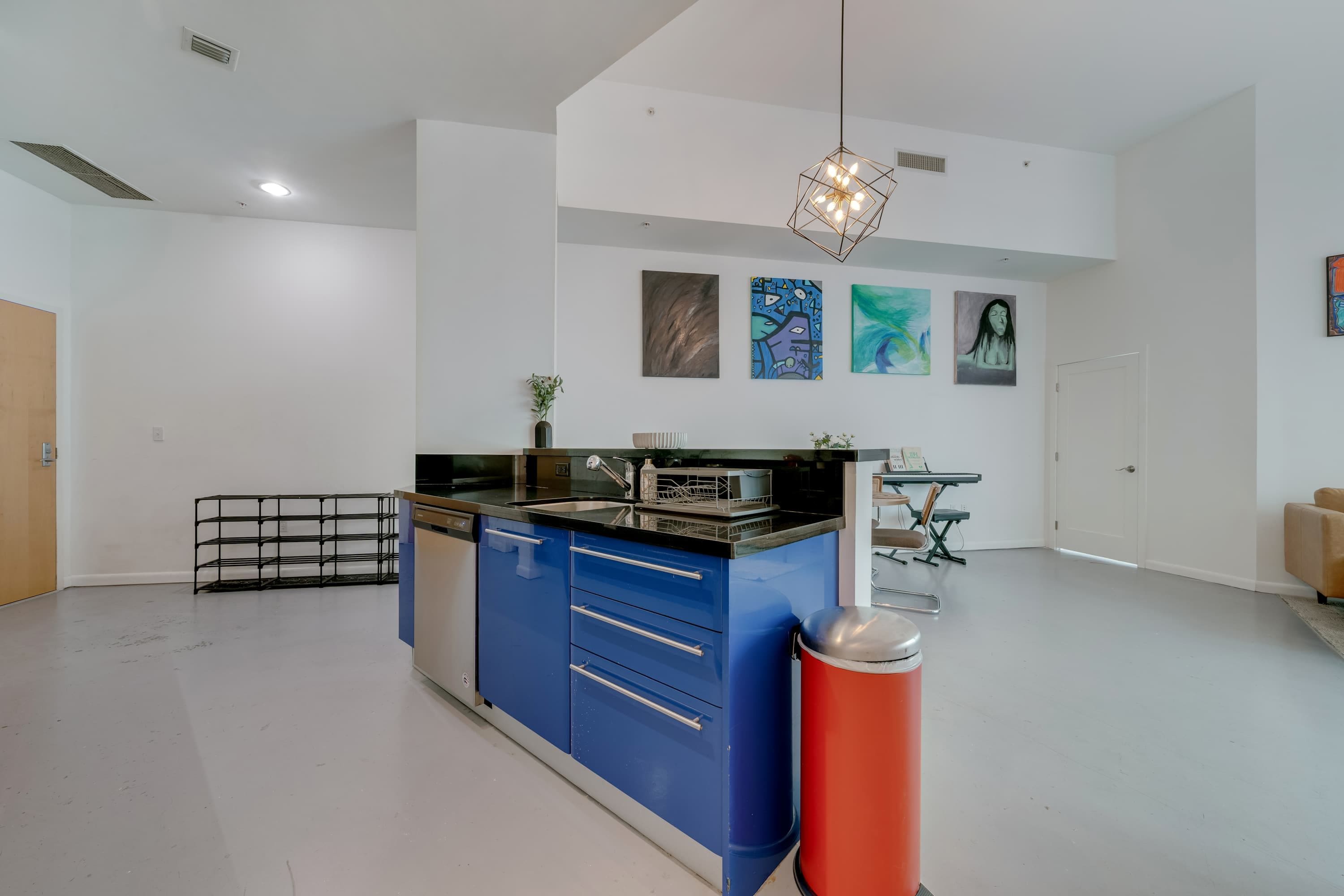 Una cocina moderna con armarios azules, encimera negra y un cubo de basura rojo.