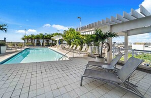 Un área de piscina en la azotea con sillones reclinables y una pérgola.