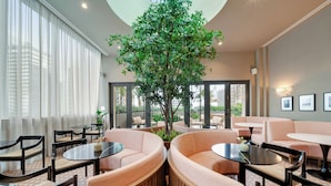 A modern lounge area with round seating, a central tree, and large windows. - Sky Sanctuary With Rooftop Pool & Hot tub (Miami)