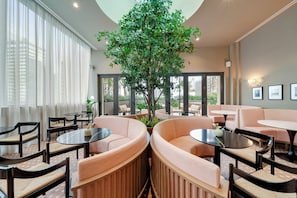 A modern lounge area with round seating, a central tree, and large windows. - Sky Sanctuary With Rooftop Pool & Hot tub (Miami)