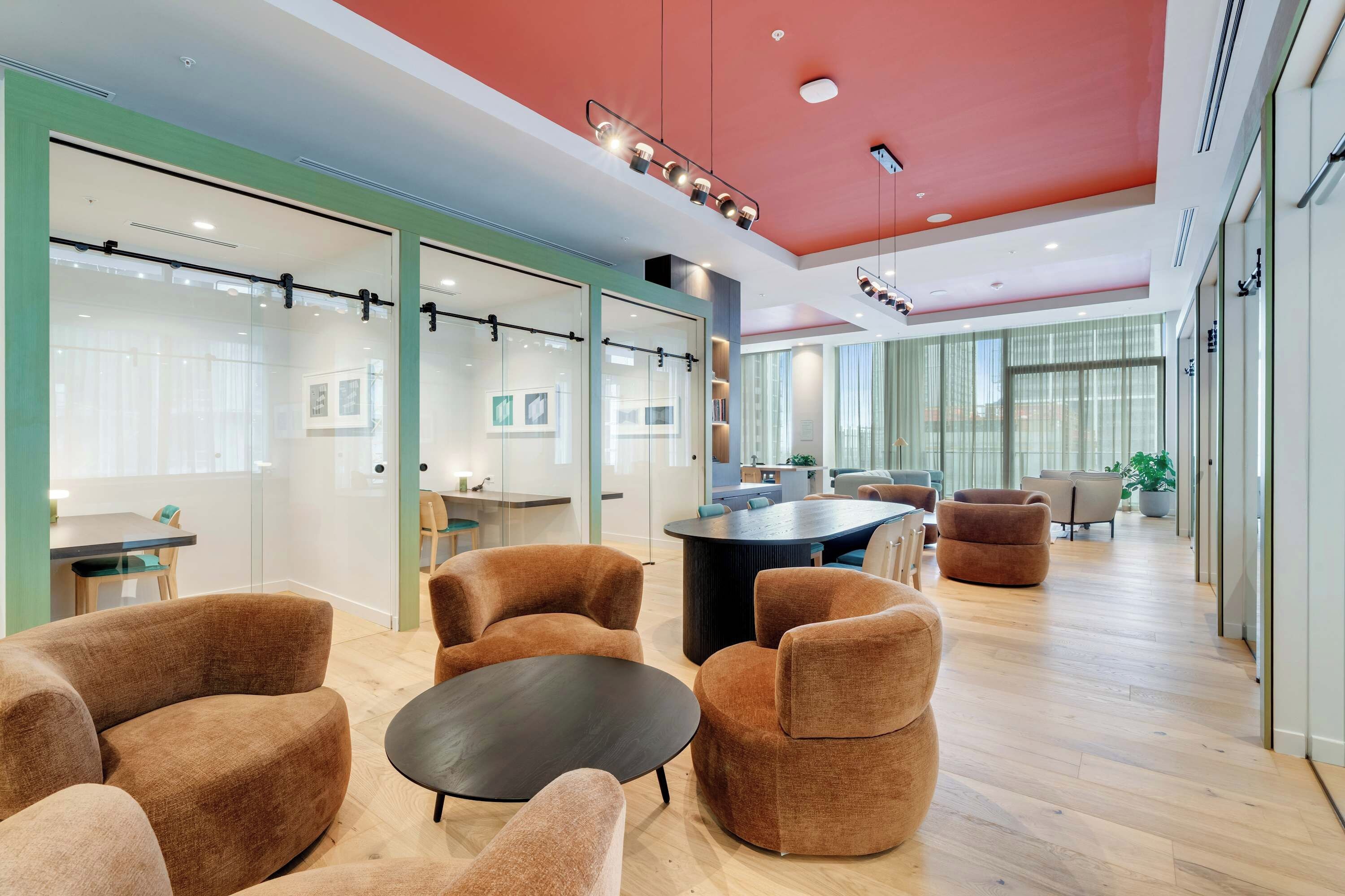 A modern office space with glass partitions, brown upholstered chairs, a central black table, and a red ceiling.