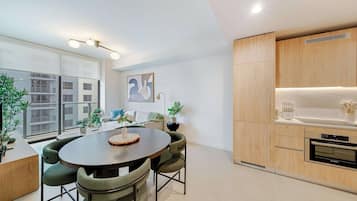 A modern kitchen with wooden cabinets, a built-in oven, and a dining area with a round table and green upholstered chairs.