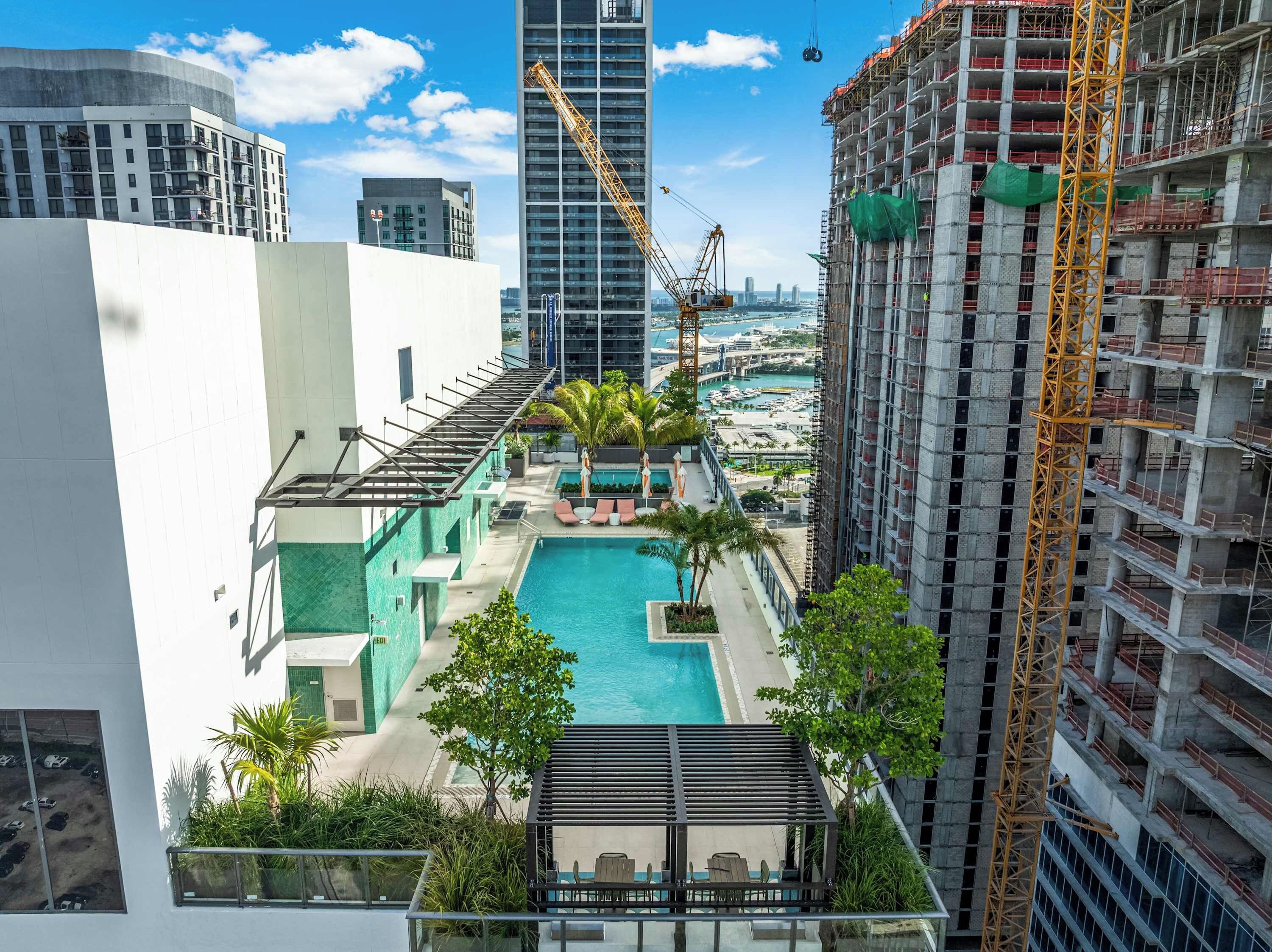 A rooftop pool with lounge chairs and a view of a cityscape, including a construction crane.