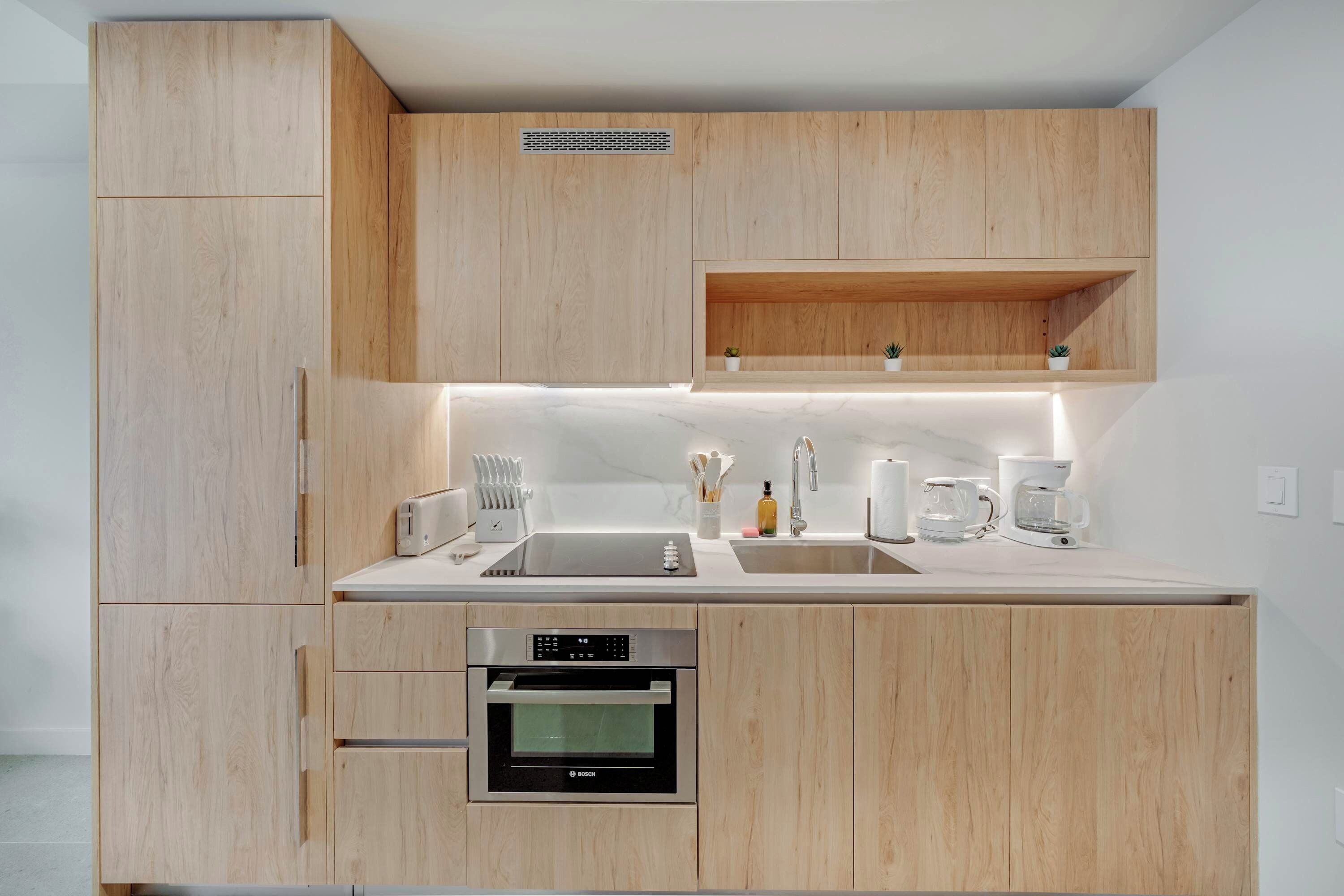 A modern kitchen with wooden cabinets, a built-in oven, a sink, and a coffee maker.