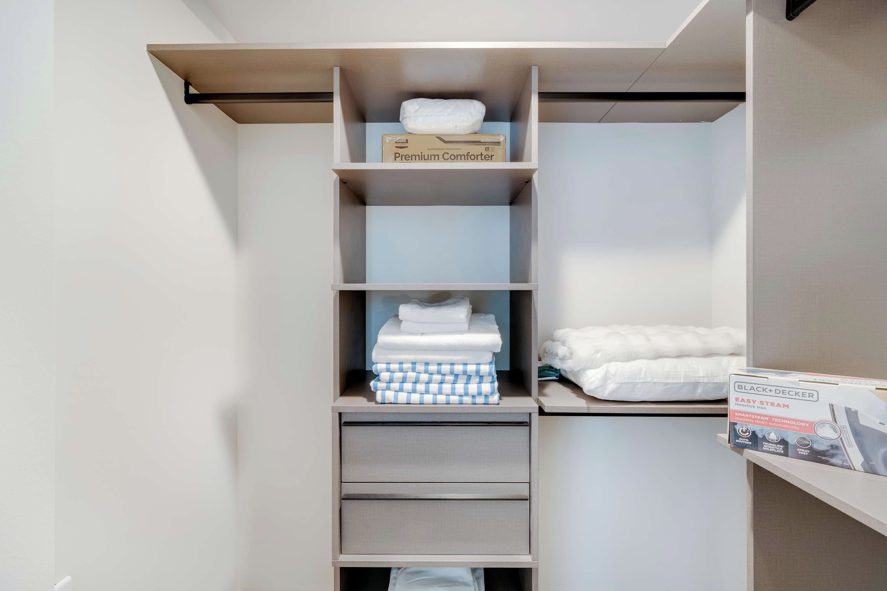 A closet with shelves and drawers, containing folded towels and a box labeled "Premium Comforter."