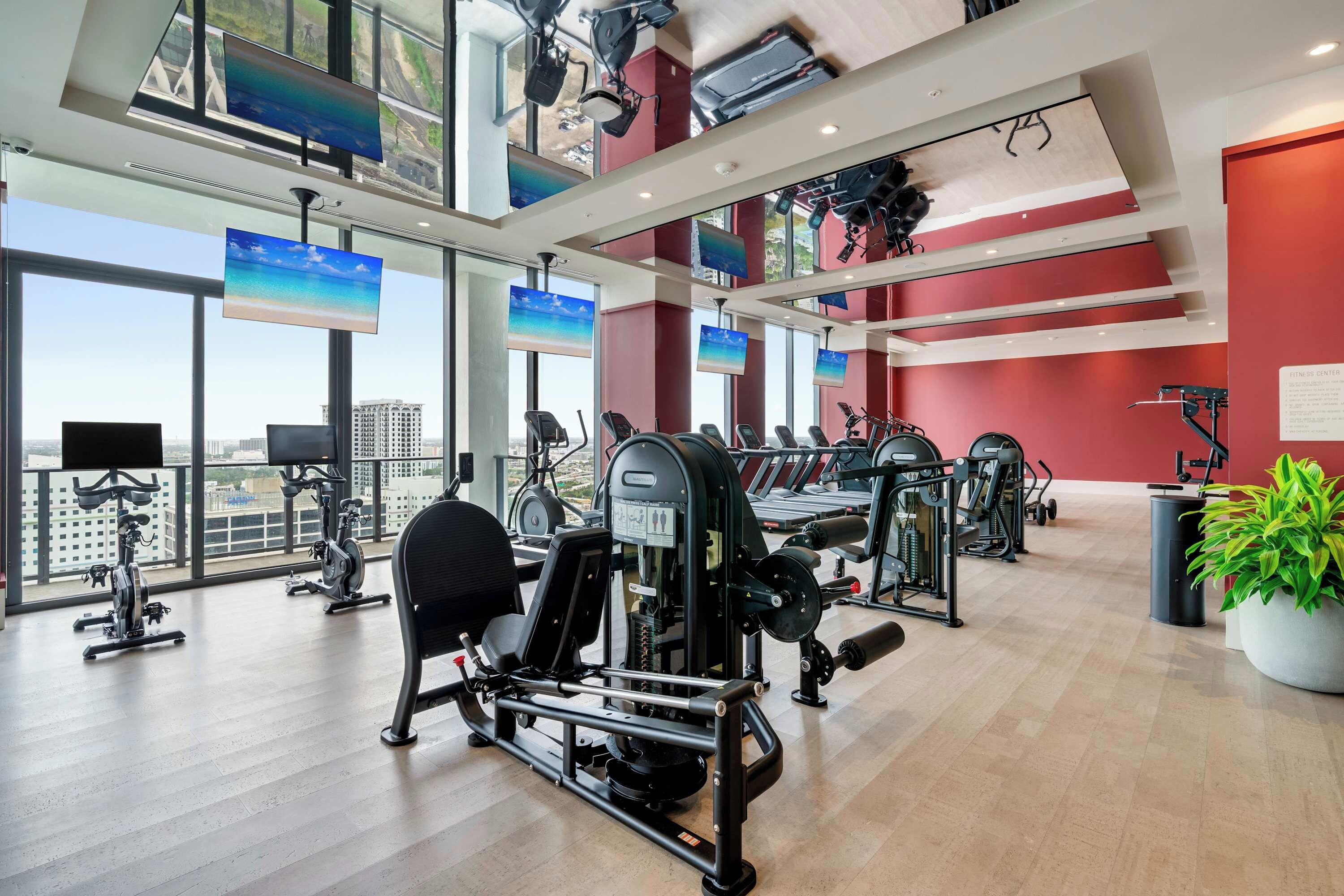 A gym with various exercise machines, large windows, and a view of the city.