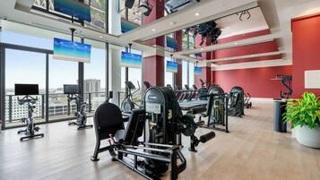A gym with various exercise machines, large windows, and a view of the city.