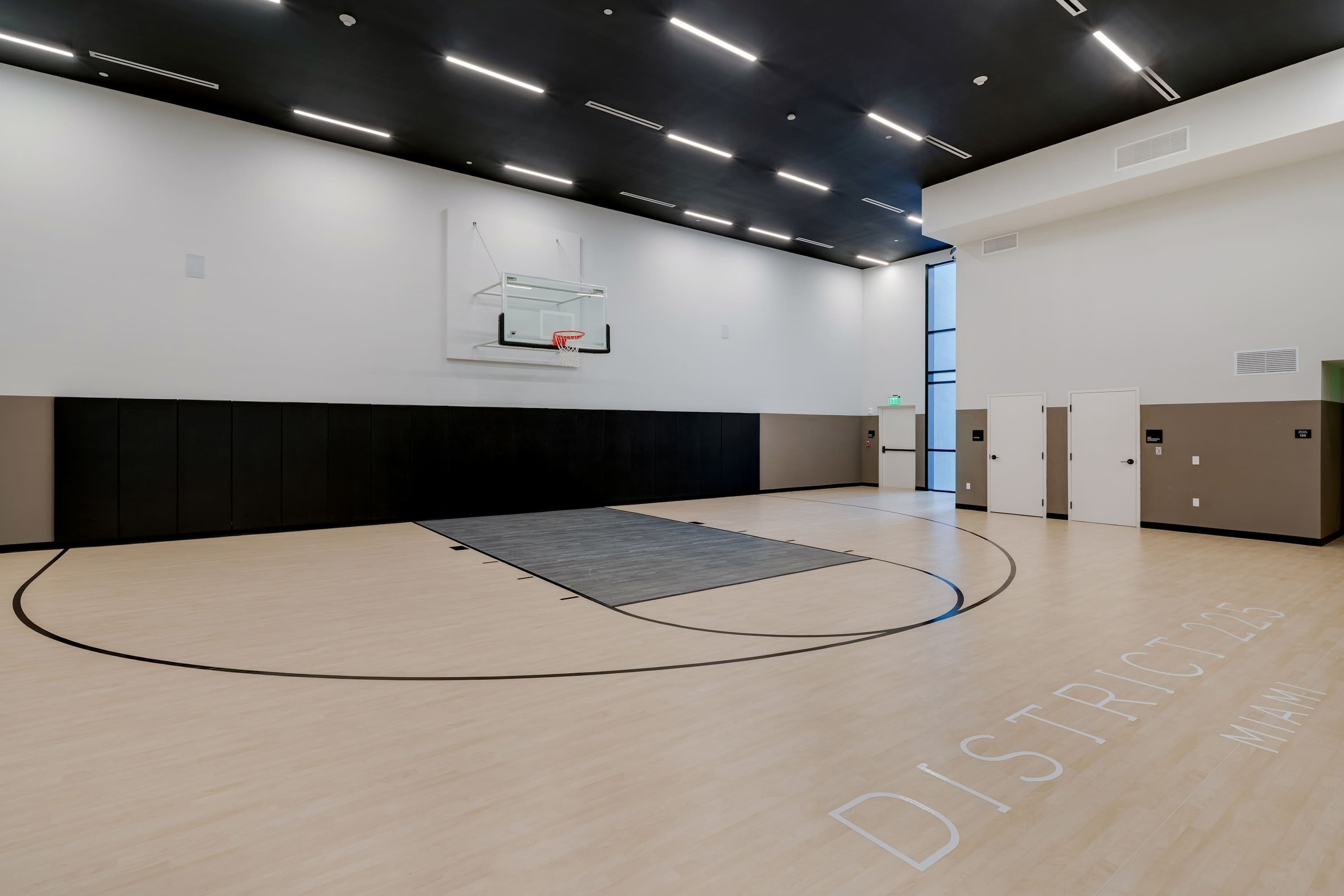 A basketball court with a hoop, a padded wall, and lockers.