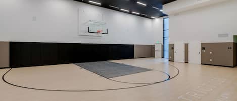 A basketball court with a hoop, a padded wall, and lockers.