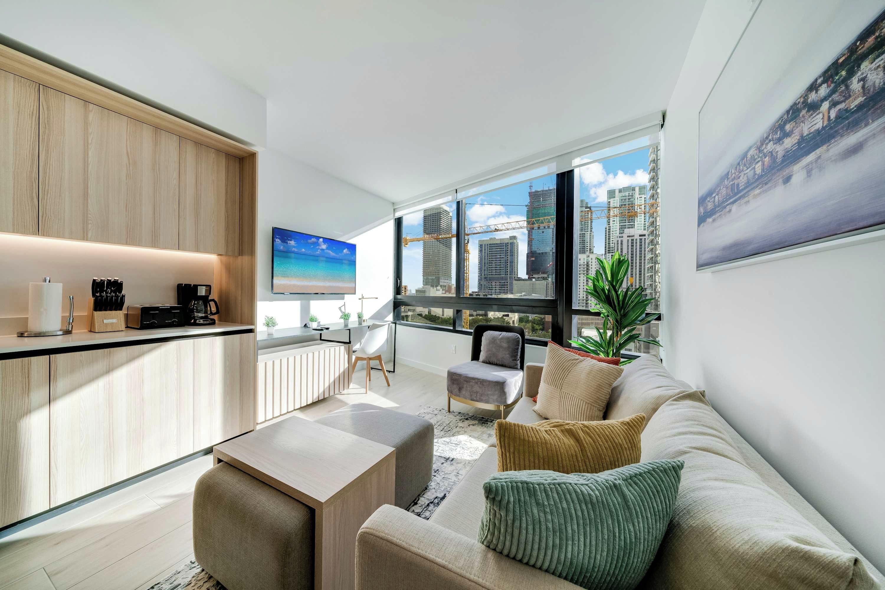 A modern living room with a sofa, coffee table, and a view of the city through large windows.
