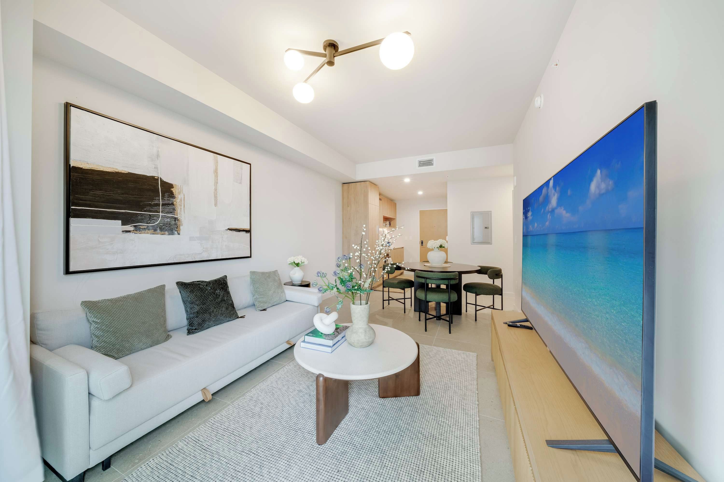 A modern living room with a white sofa, a round coffee table, and a large painting of a beach scene.