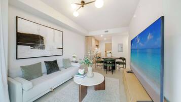 A modern living room with a white sofa, a round coffee table, and a large painting of a beach scene.