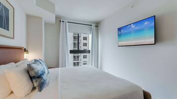 A hotel room with a bed, a painting of a beach, and a view of a building through a window.