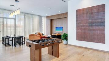 A modern room with a wooden foosball table, a dining area with black chairs, and a large abstract painting on the wall.