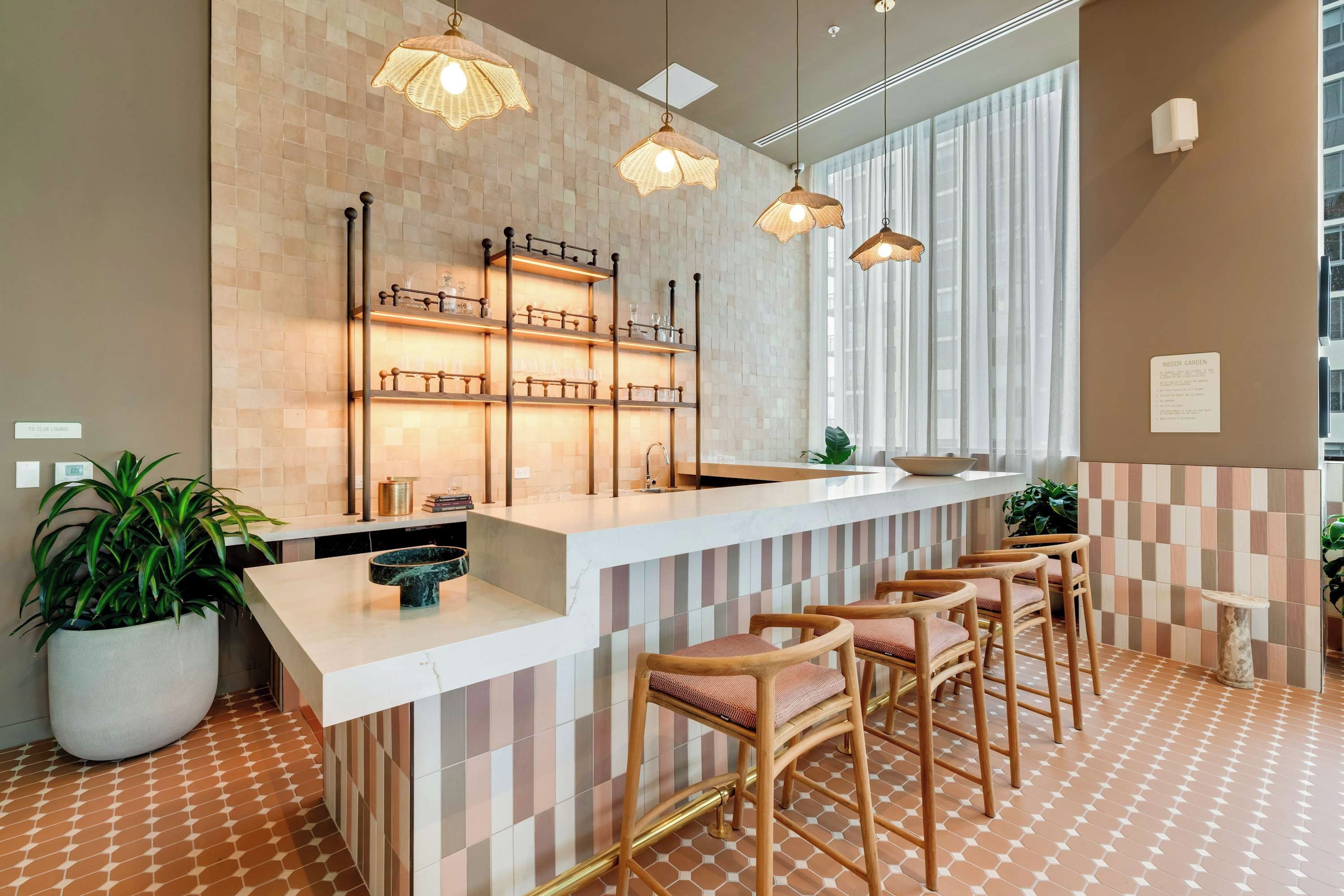 Una cocina moderna con barra, taburetes de madera, iluminación colgante y una planta grande en maceta.