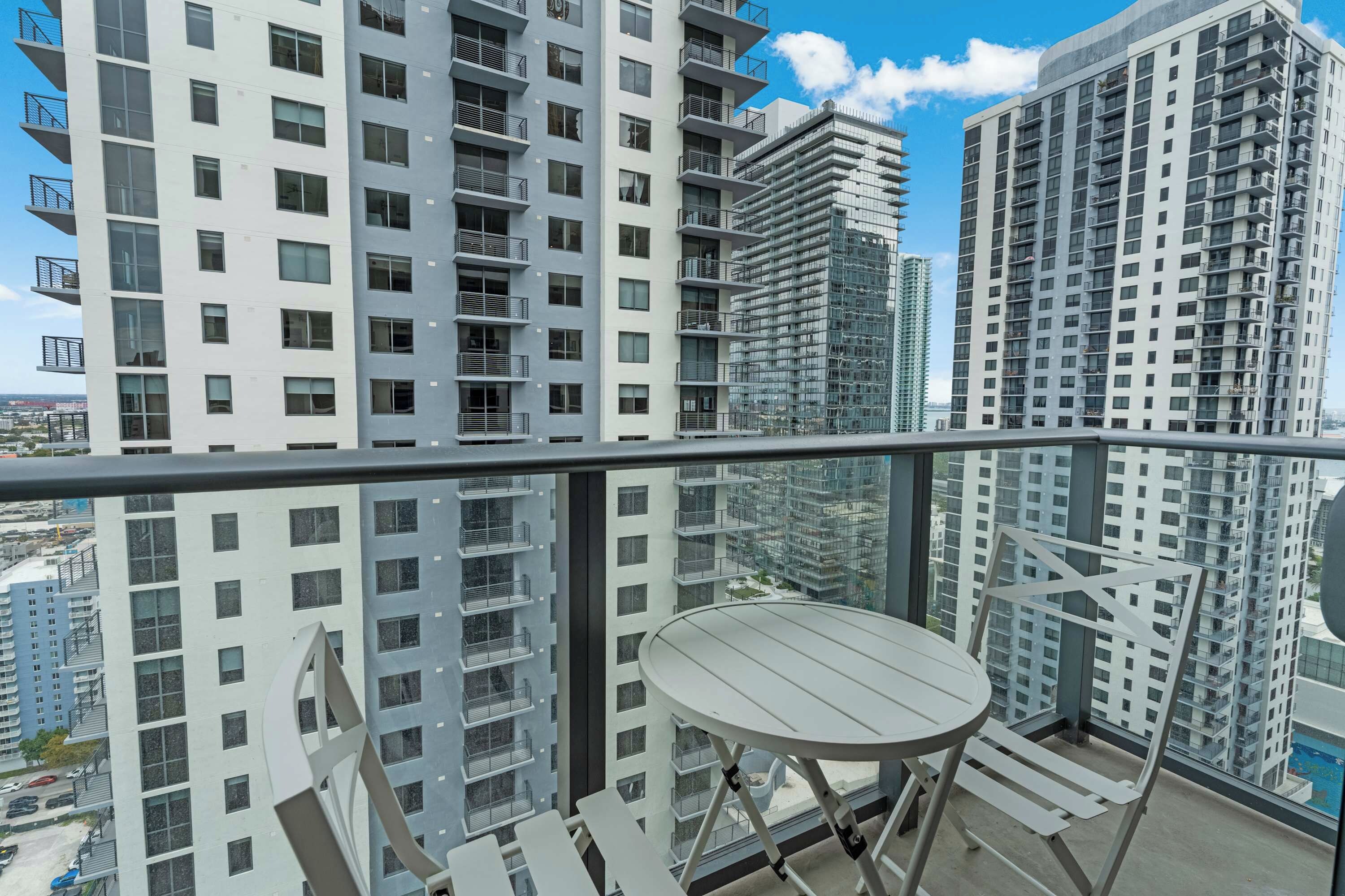 A balcony with a table and chairs, overlooking high-rise buildings and a cityscape.