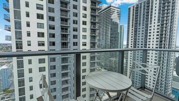 A balcony with a table and chairs, overlooking high-rise buildings and a cityscape.